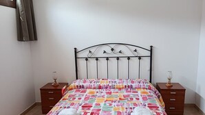 A bedroom with a bed, two nightstands, a window with curtains, and a wall-mounted lamp. - Atalaya 4001 Ground-Floor Apartment (Arnuero)