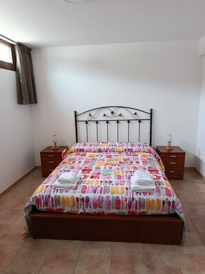 A bedroom with a bed, two nightstands, a window with curtains, and a wall-mounted lamp. - Atalaya 4001 Ground-Floor Apartment (Arnuero)