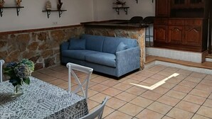 A living area with a stone wall, a blue sofa, a dining table with chairs, and a kitchen area with wooden cabinets. - Atalaya 4001 Ground-Floor Apartment (Arnuero)