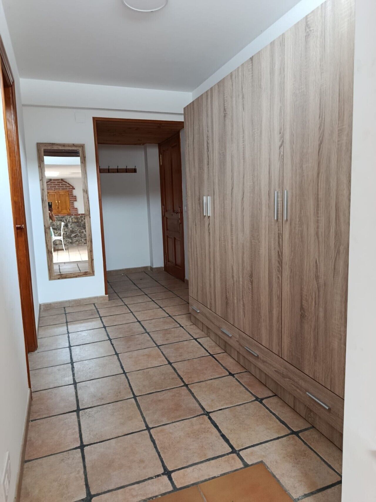 Un couloir doté d’un sol carrelé, d’une armoire en bois et d’une porte-fenêtre donnant sur une autre pièce.