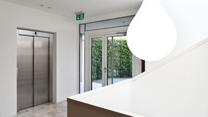 Um elevador moderno e uma porta de vidro que dá para uma área externa com vegetação.