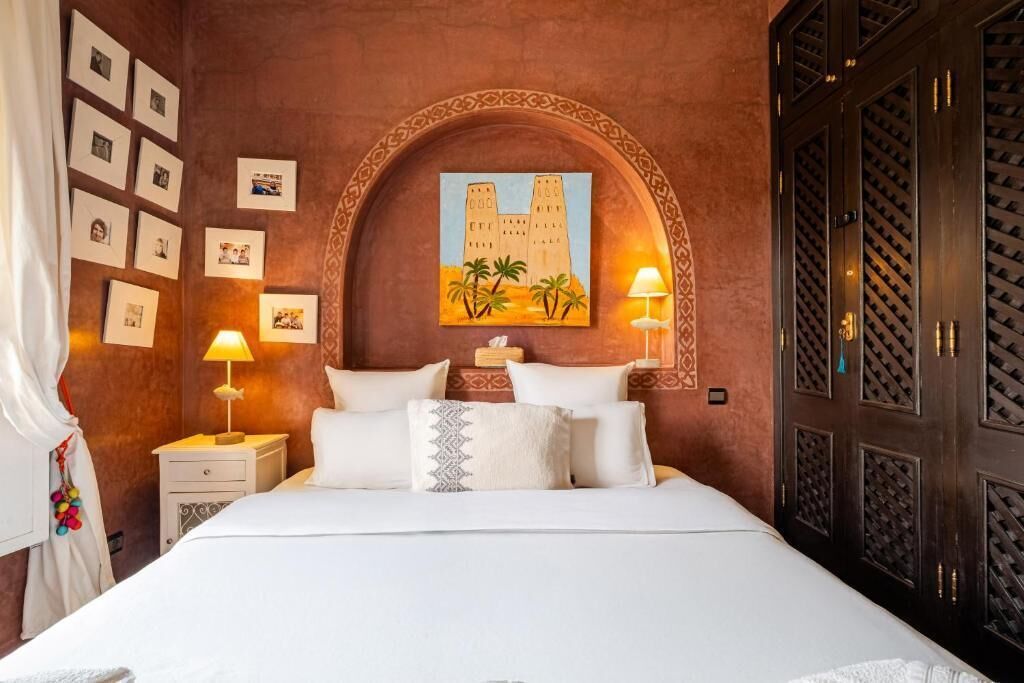 A hotel room with a large bed, two bedside lamps, a wall-mounted painting, and a wardrobe with a patterned door.