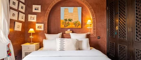 A hotel room with a large bed, two bedside lamps, a wall-mounted painting, and a wardrobe with a patterned door.