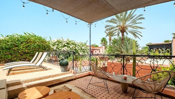 An outdoor patio with a table and chairs, a hammock, and a view of the surrounding greenery and buildings. - Riad Khiata (Marrakech)