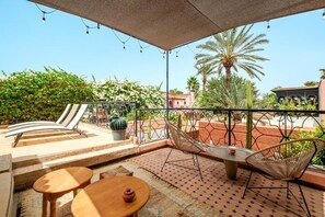 Un patio exterior con mesa y sillas, una hamaca y vistas a la vegetación y edificios circundantes.