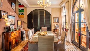 A dining area with a table set for four, a chandelier, and a view through a large window. - Riad Khiata (Marrakech)