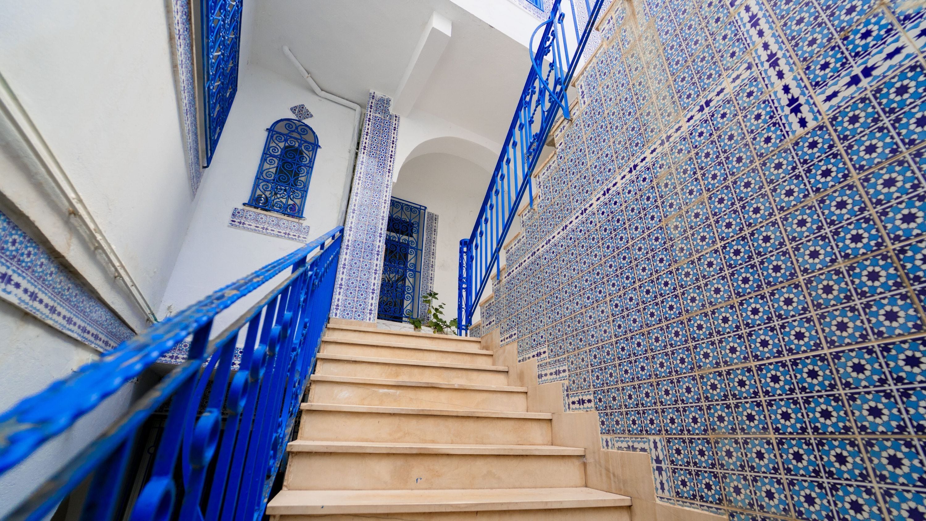 A staircase with blue railings leading to a room with a patterned wall.