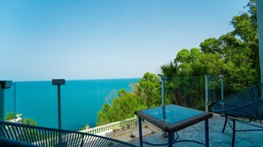 A balcony with a glass table and chairs overlooking a coastal view. - Le Paradis Bleu Luxueux Duplex Avec vue mer (Sidi Bou Said)