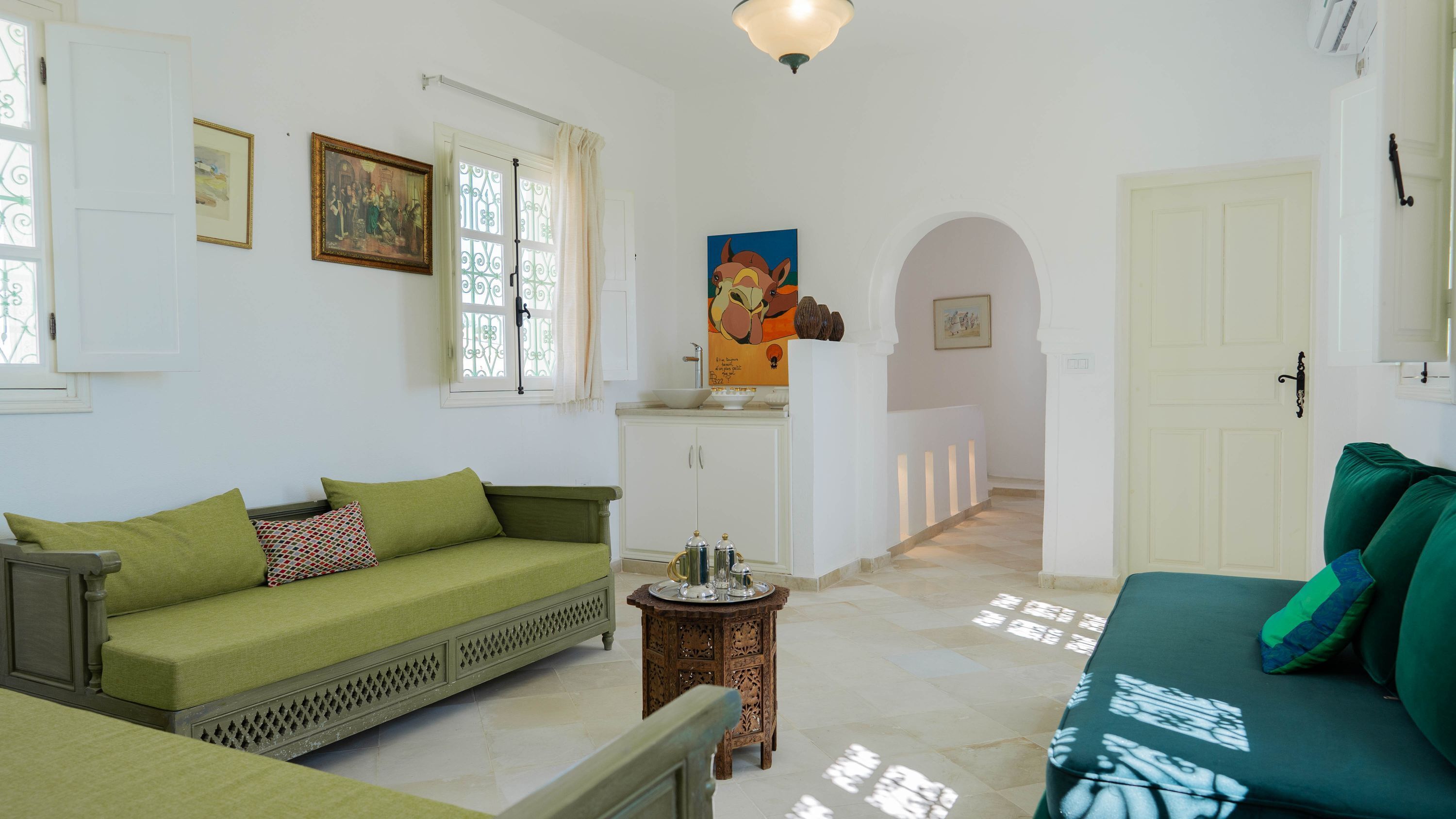 Una habitación con un sofá verde, una mesita de madera, un armario blanco y un cuadro en la pared.