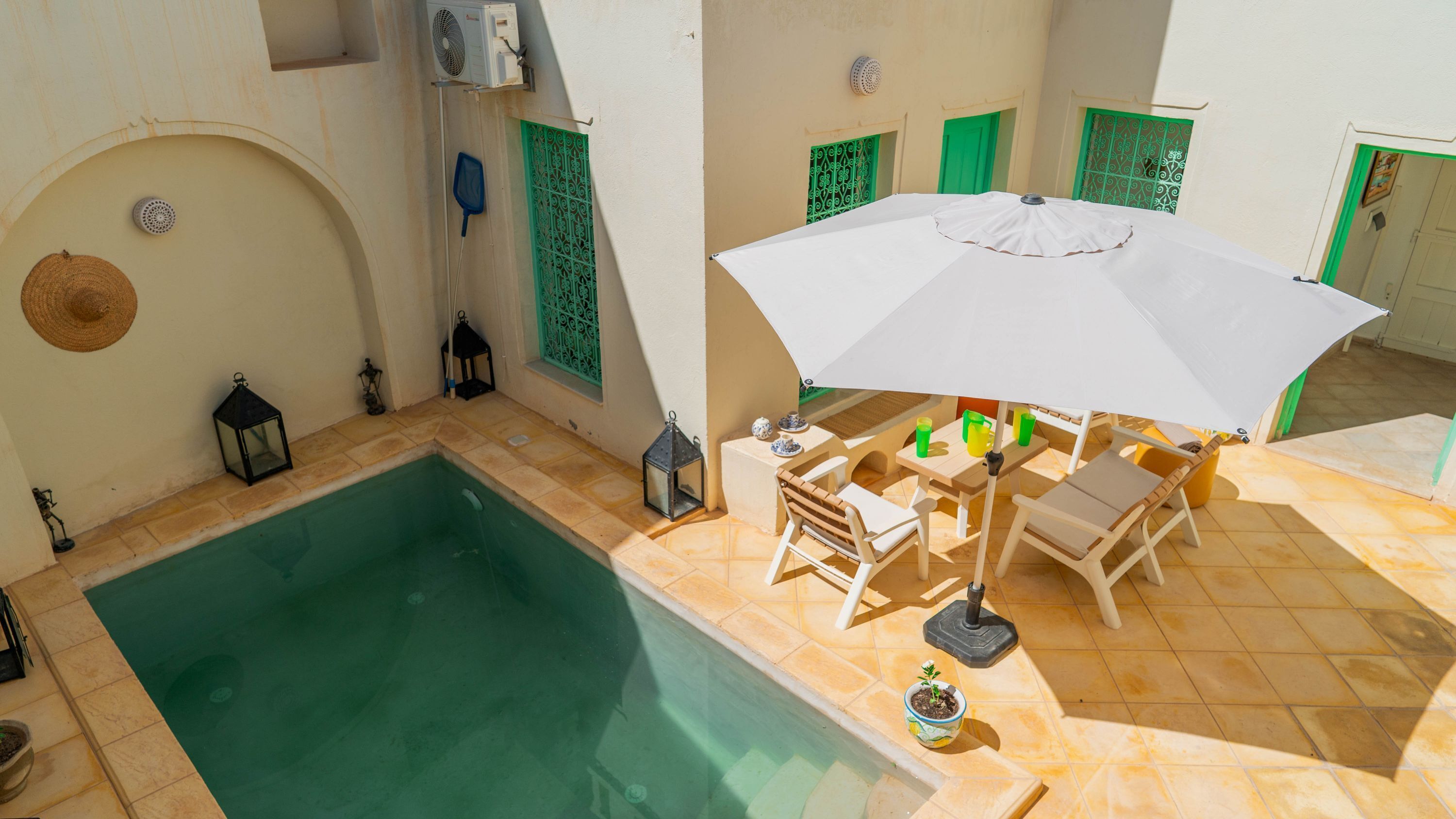 A poolside area with a table and chairs under a white umbrella, a small pool, and decorative lanterns.