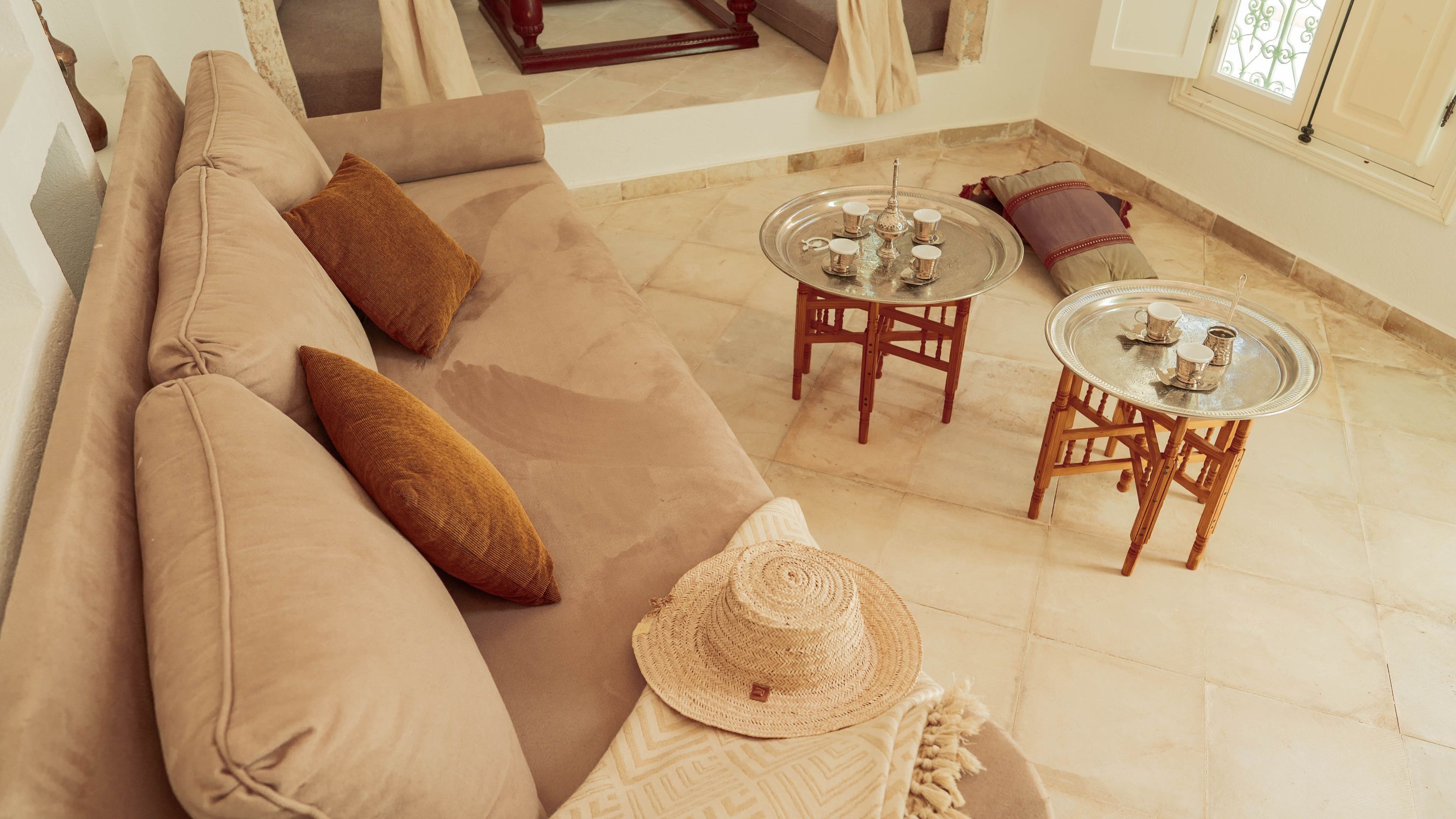 Un salon moderne avec un canapé beige, deux petites tables rondes et un chapeau en fibres tressées.