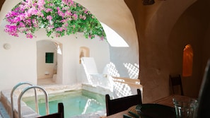 A sunlit pool area with a chair and a table, surrounded by white walls and arches. - Dar Dada Djerba Maison Traditionnelle Houch (Erriadh)