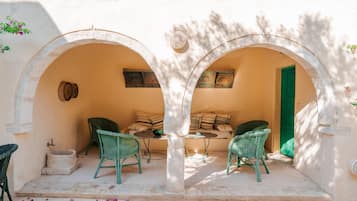 A cozy outdoor seating area with two green wicker chairs and a small table, under a white archway.