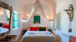 Una habitación con cama, ventana, espejo y una lámpara fijada a la pared.