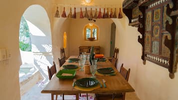 Comedor con mesa de madera dispuesta para seis personas, rodeada de sillas, una ventana y elementos decorativos.
