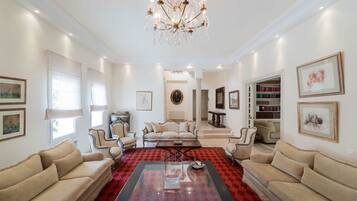 A spacious living room with a chandelier, multiple seating areas, and a red patterned rug.