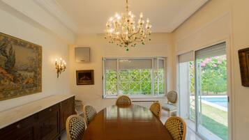 Une salle à manger avec une grande table en bois, entourée de chaises en osier, d’un lustre et d’un tableau accroché au mur.
