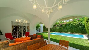 An outdoor patio with a wooden table and wicker furniture, a pool, and a view of a garden. - Villa d Exception Gammarth Piscine Priv e (La Marsa)