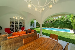 An outdoor patio with a wooden table and wicker furniture, a pool, and a view of a garden. - Villa d Exception Gammarth Piscine Priv e (La Marsa)