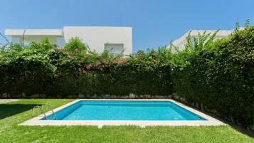 A rectangular swimming pool with a metal ladder, surrounded by well-maintained grass and dense foliage.