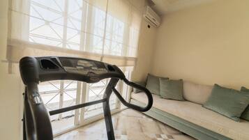 A stationary exercise bike in a room with a large window, a sofa, and a tiled floor.