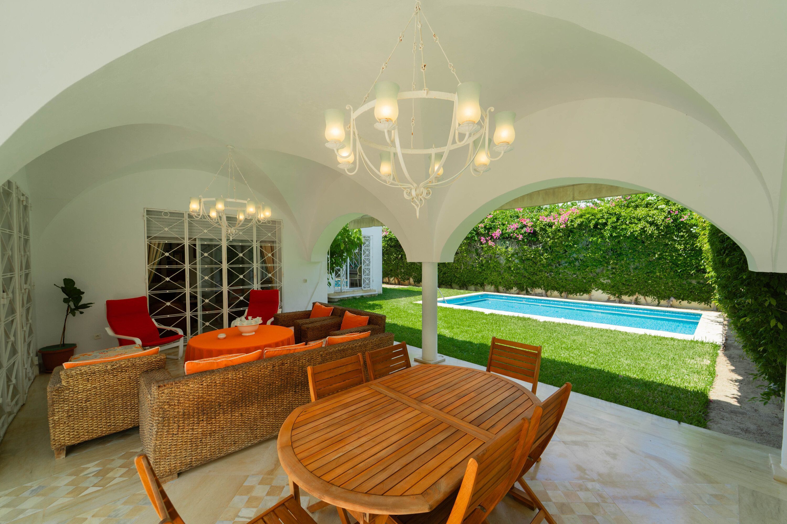 Une terrasse extérieure avec une piscine, des meubles en osier et une structure de plafond blanche.