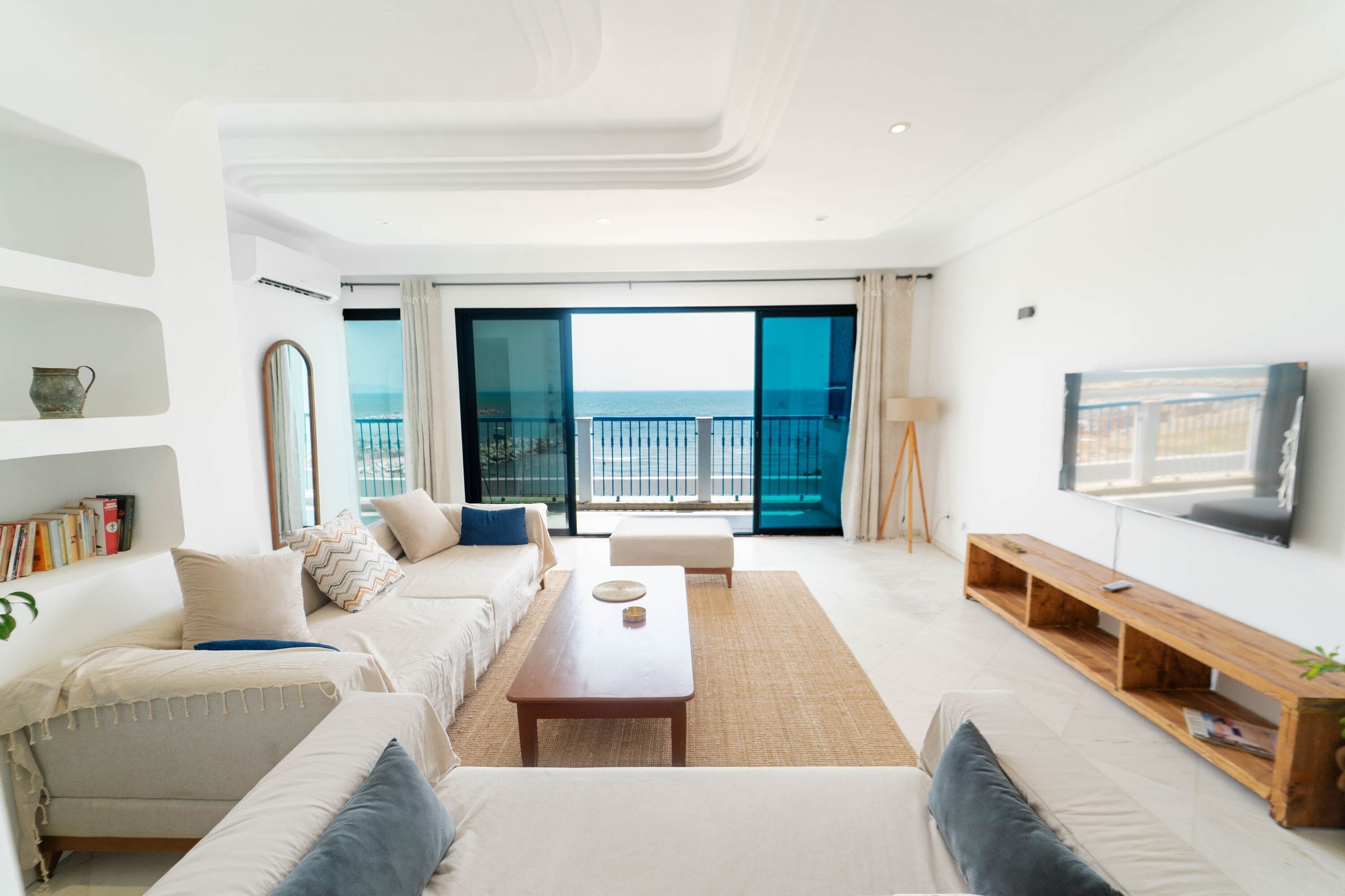 Un salon moderne comprenant un ensemble de canapés, une table basse, un téléviseur et un balcon avec vue sur la mer.