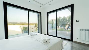 Un dormitorio moderno con una cama grande, dos ventanas y vistas a un lago y colinas.