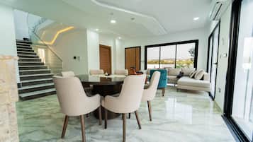 A modern living room with a glass dining table, beige sofas, and a staircase leading to an upper level.