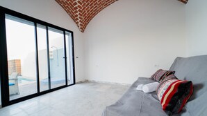 Ein modernes Wohnzimmer mit grauem Sofa, einem gemusterten Überwurf und Blick auf einen Swimmingpool durch eine Glastür.
