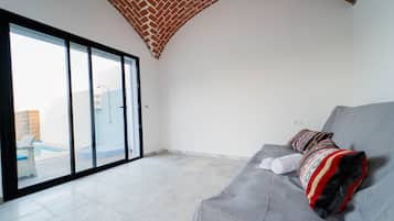 Una sala de estar moderna con un sofá gris, una manta estampada y vistas a una piscina a través de un ventanal.