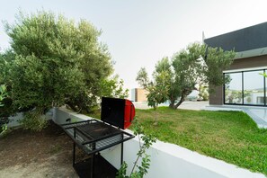 Ein moderner Außenbereich mit Grill, einem kleinen Baum und einem Gebäude mit großen Fenstern.