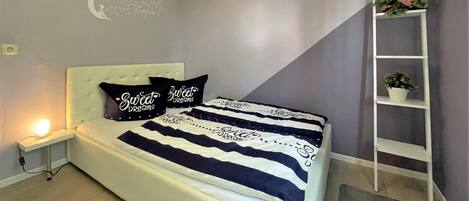 A bedroom with a bed, bedside table, wall decor, and a white shelving unit.