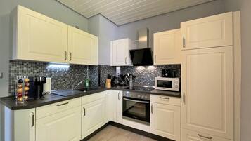 A modern kitchen with white cabinets, a black countertop, a microwave, and a stove.