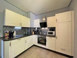 A modern kitchen with white cabinets, a black countertop, a microwave, and a stove. - SweetDreams Holiday Home – Terrace, Garden, Wi-Fi, Dogs Welcome – Private Guests Only (Bad Sachsa)
