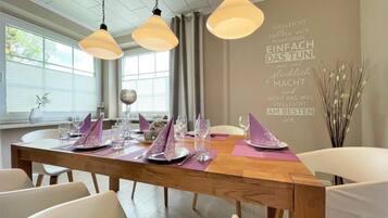 A dining area with a wooden table set for four, white chairs, and pendant lighting.