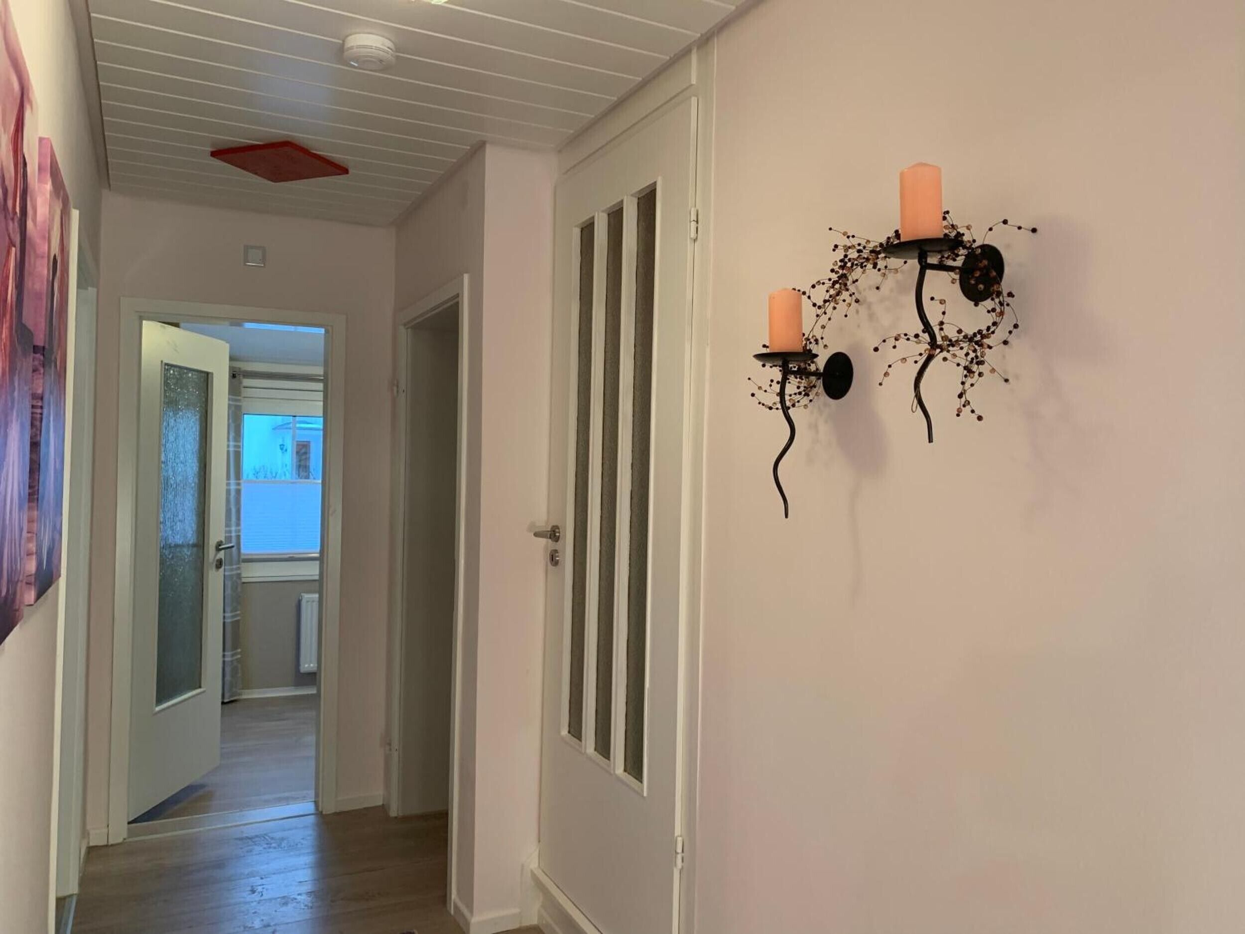 A hallway with a door, a wall-mounted candle holder with two candles, and a ceiling vent.