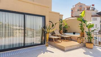 Une terrasse sur le toit avec une porte vitrée, des chaises longues, une petite piscine et des plantes en pot.