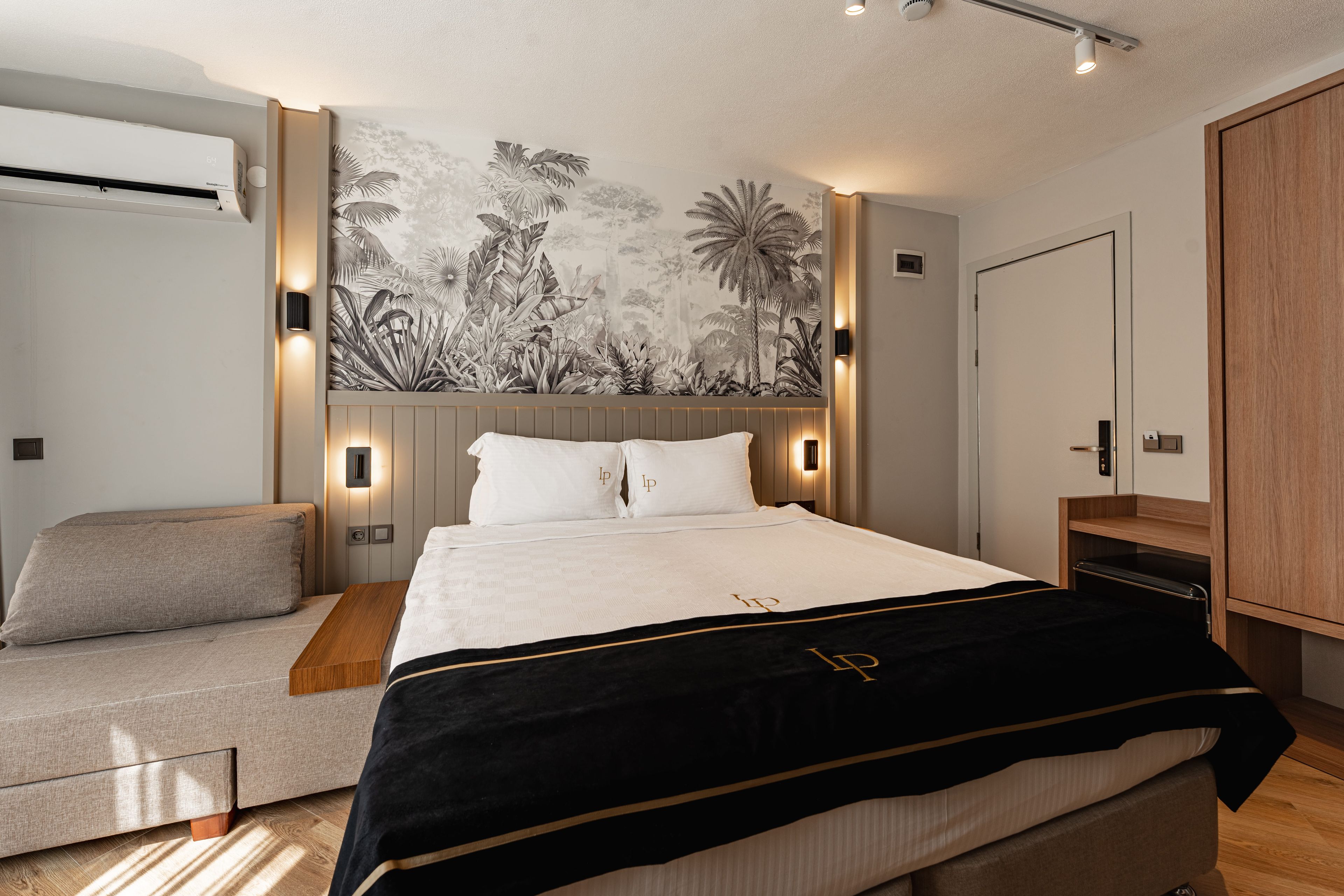 A modern bedroom with a bed, a sofa, a wardrobe, and a wall with a tropical mural.