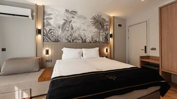 A modern bedroom with a bed, a sofa, a wardrobe, and a wall with a tropical mural.