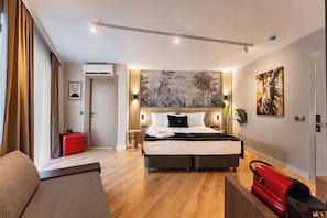 A hotel room with a bed, a red suitcase, a plant, and a painting on the wall.