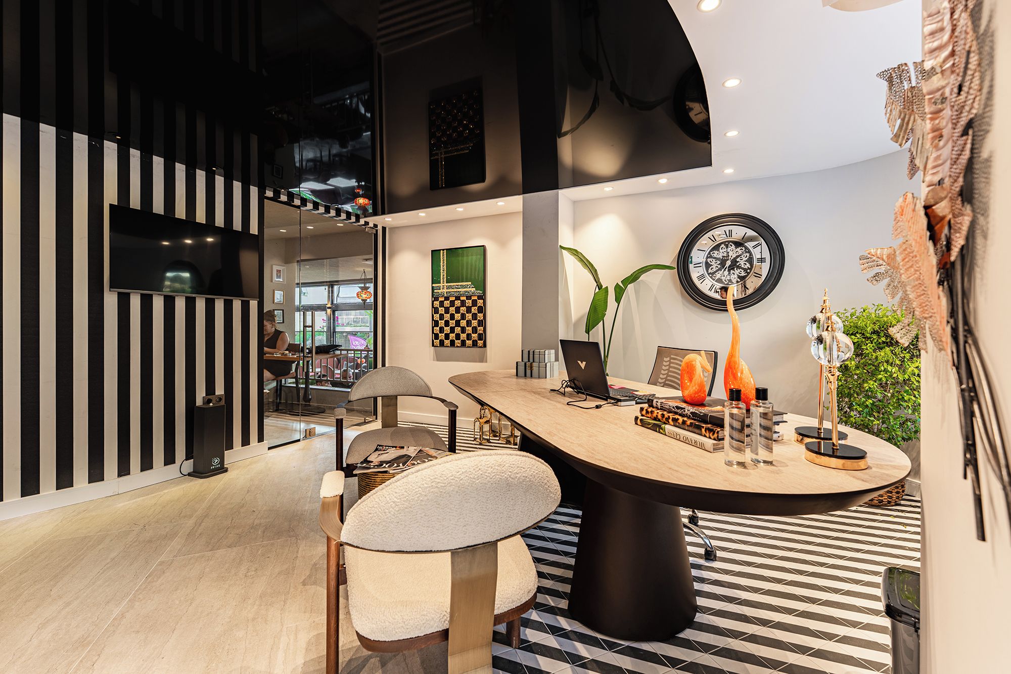 A modern interior with a round table, chairs, a laptop, decorative items, and a clock on the wall.
