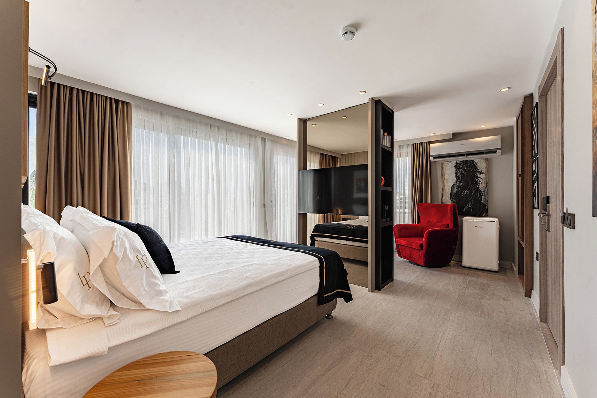 A hotel room with a bed, a TV, a red chair, and a small table.