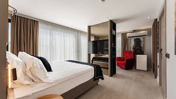 A hotel room with a bed, a TV, a red chair, and a small table.