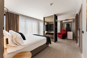 A hotel room with a bed, a TV, a red chair, and a small table. - LOOKS PRIVE SUITES (Antalya)
