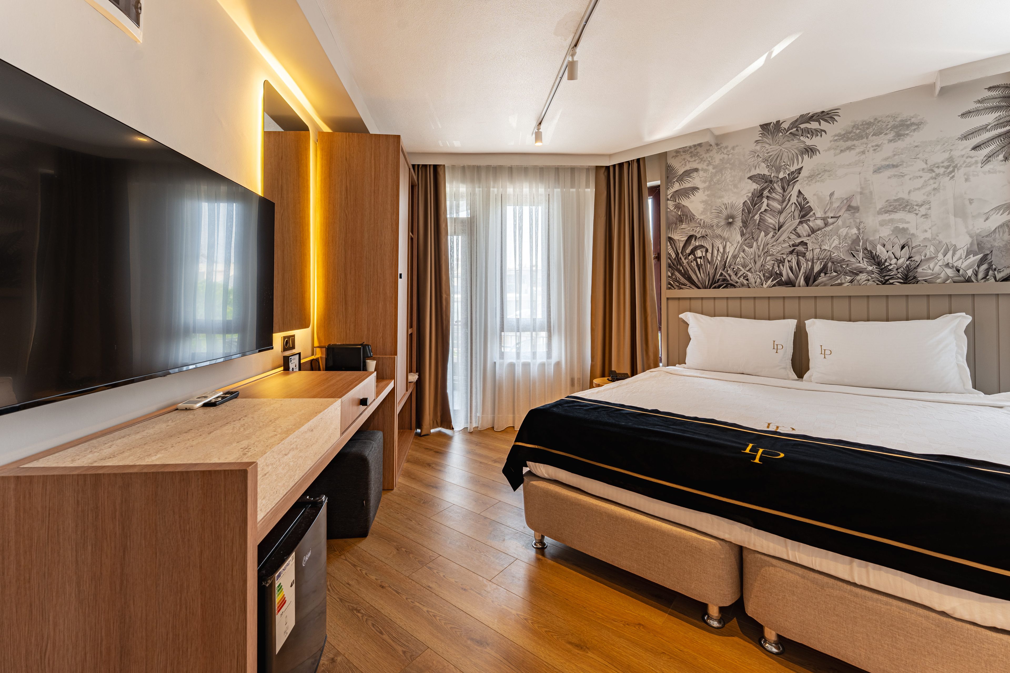 Ein Hotelzimmer mit Bett, Schreibtisch, Fernseher und einer Wand mit einem tropischen Wandbild.