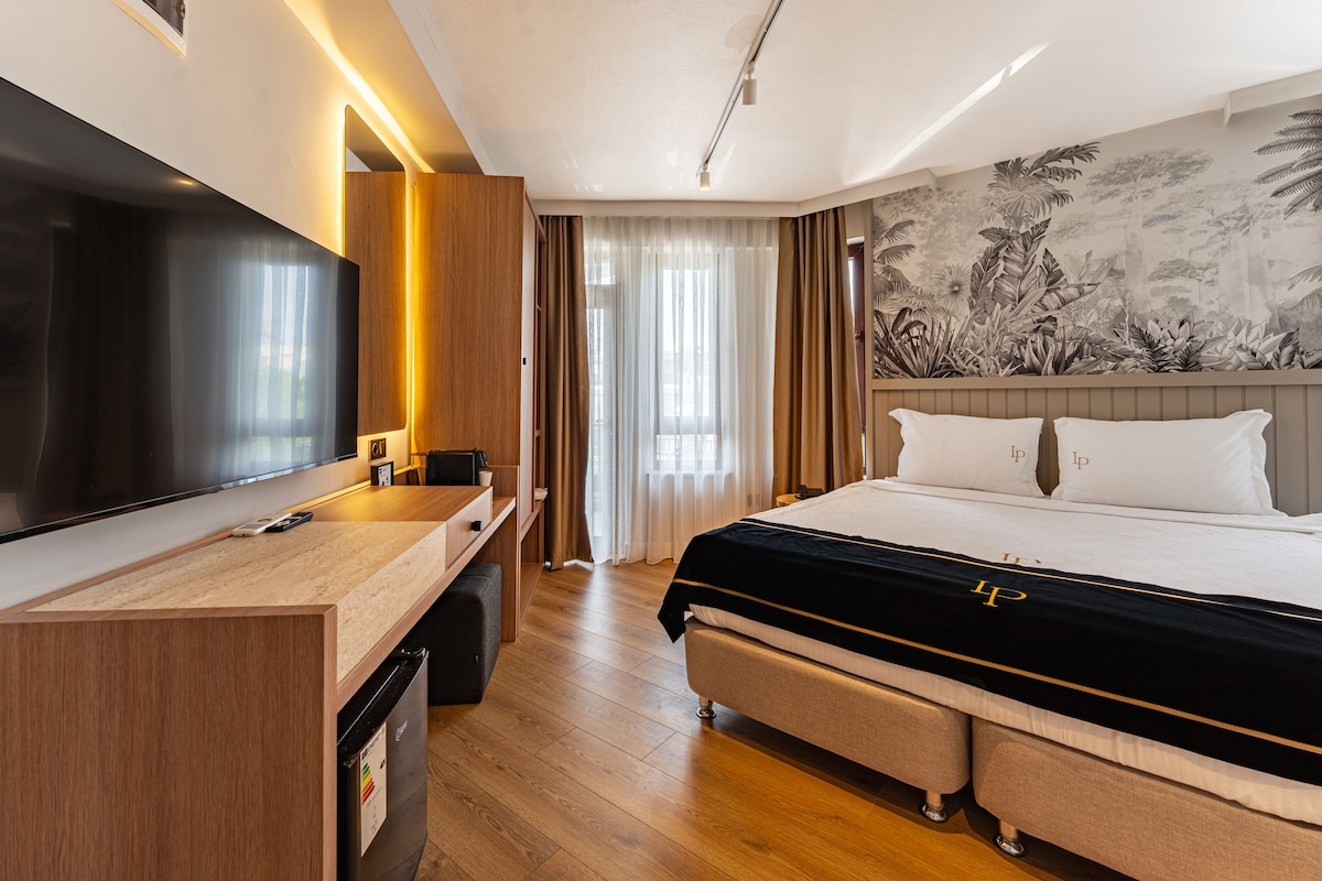 Habitación de hotel con cama, escritorio, televisión y un mural tropical en la pared.
