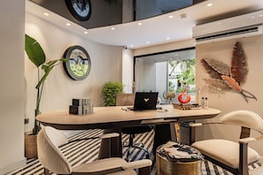 Un espace de bureau moderne comprenant une table ronde, deux chaises, un ordinateur portable et des éléments de décoration, notamment une horloge murale et une plante fixée au mur.