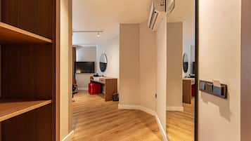 A modern room with a wooden floor, a built-in wardrobe, a desk with a chair, a small trash bin, and a mirror on the wall.