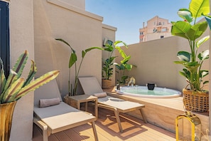 Une terrasse sur le toit équipée d’un jacuzzi, de chaises longues et de plantes en pot.